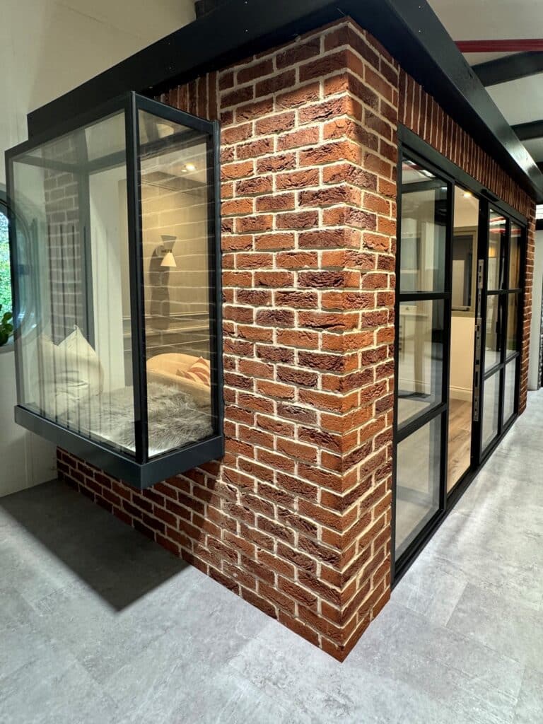 Brick Brick‑red Pillar with Black Metal and Large Glass Panels Forming a Modern Showroom Partition.